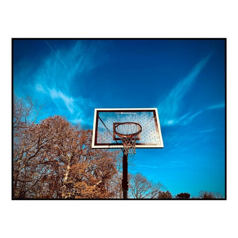 A basketball hoop shines in the sun with a blue sky behind it.