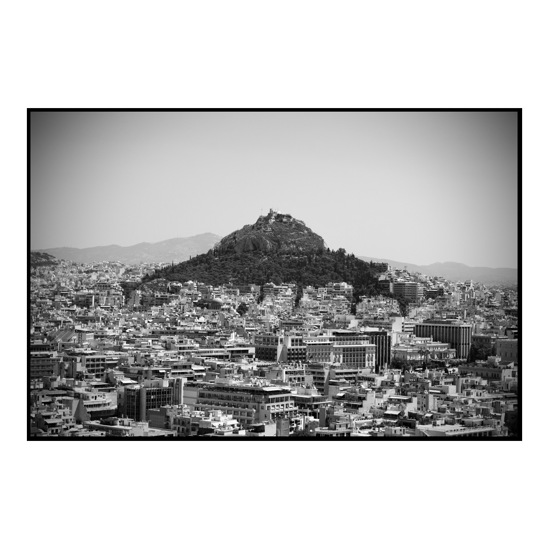 A black and white photo of the city of Athens with a mountain in the background. And lots of buildings.