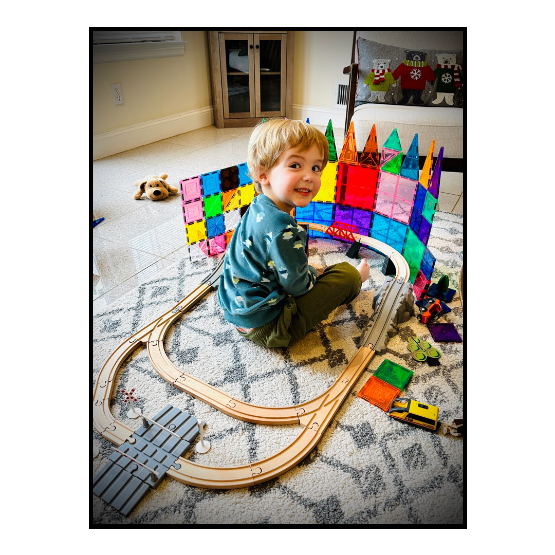 Our son sitting inside the middle of a train set and toys on the floor.