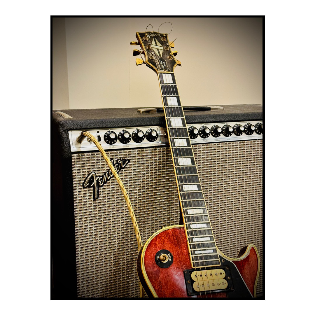 A red guitar leans against a vintage amplifier. 