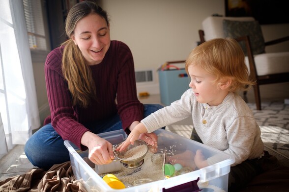 Mother and son exploring the sensory bin filled with rice and toys in some nice window light.