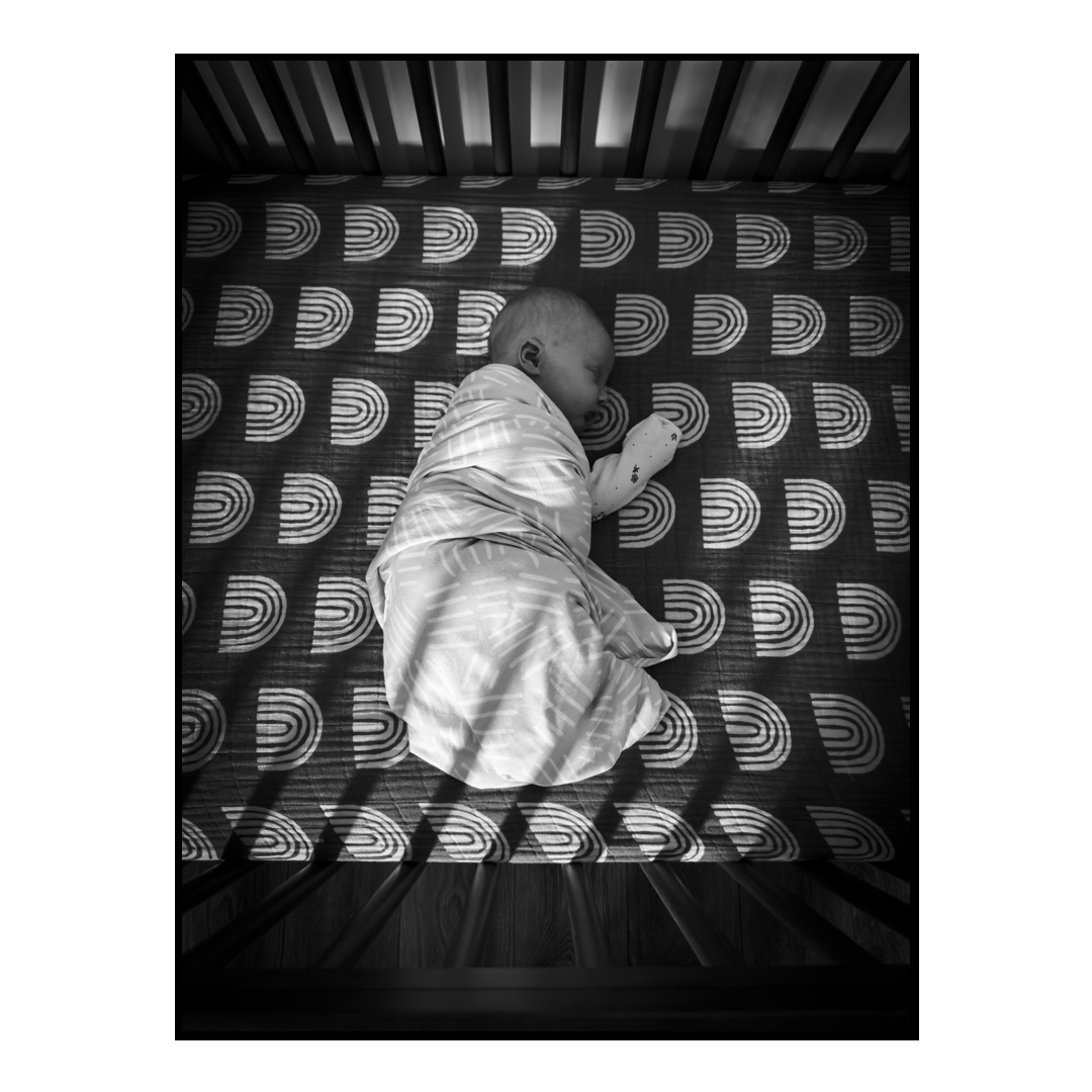 An infant lays in a crib bathed in light