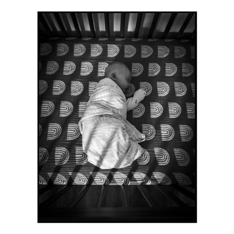 An infant lays in a crib bathed in light