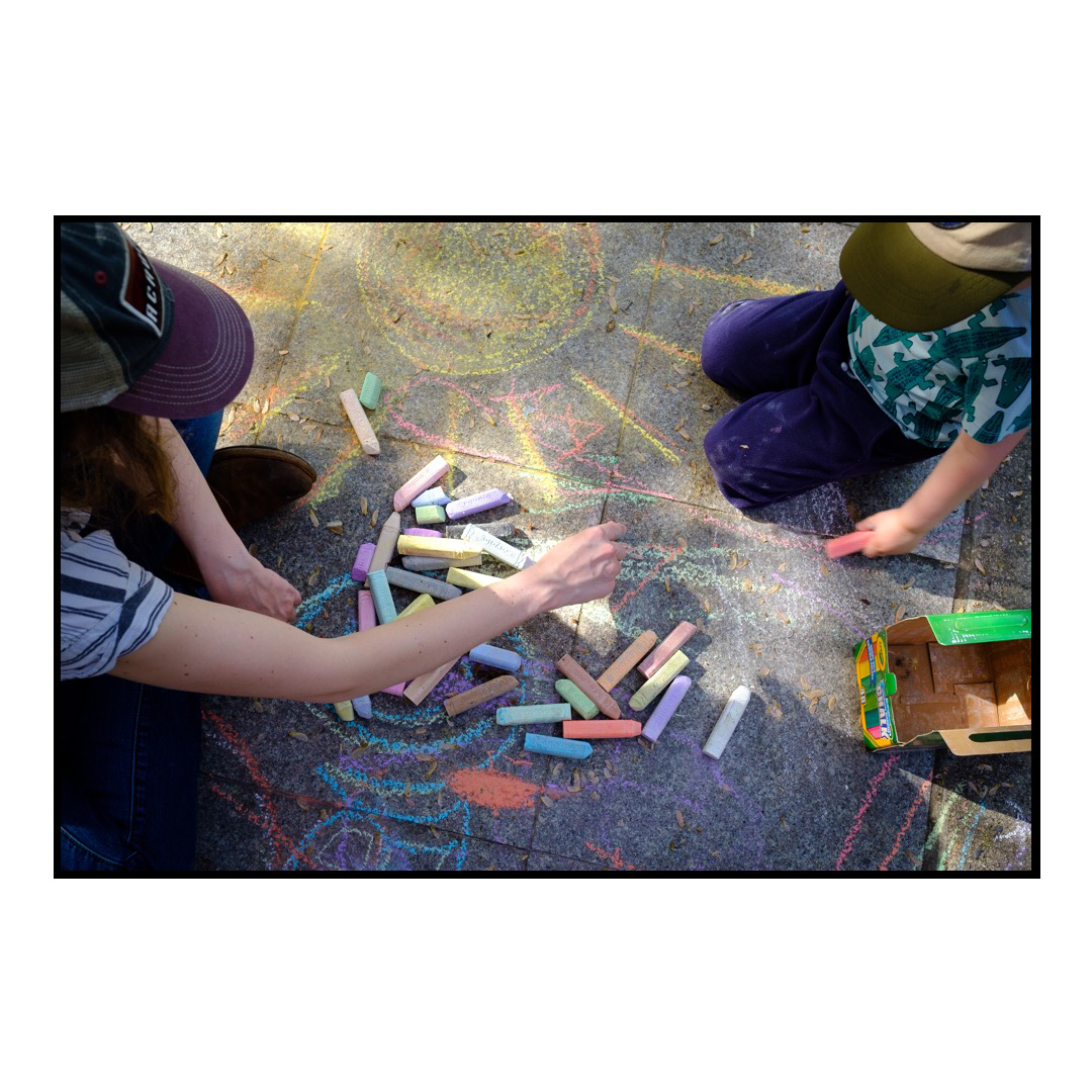 Mother and son playing with bright colored chalk on a sidewalk