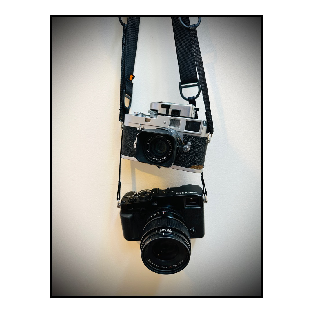 Two rangefinder cameras hang against a white wall.