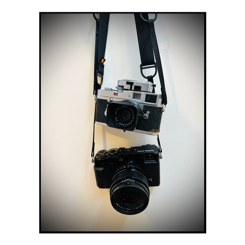 Two rangefinder cameras hang against a white wall.